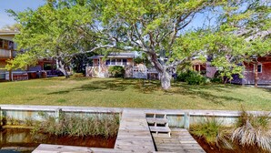 A wooden dock leading to a small pond with a tree in the center, surrounded by a grassy yard and houses. - Waterfront House w/ Water View, Shared Pool, Private Washer/Dryer, & Free WiFi (Frisco)