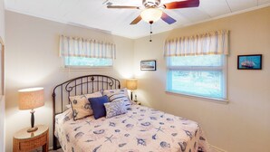 A bedroom with a bed, two bedside tables, a ceiling fan, and windows with curtains. - Waterfront House w/ Water View, Shared Pool, Private Washer/Dryer, & Free WiFi (Frisco)