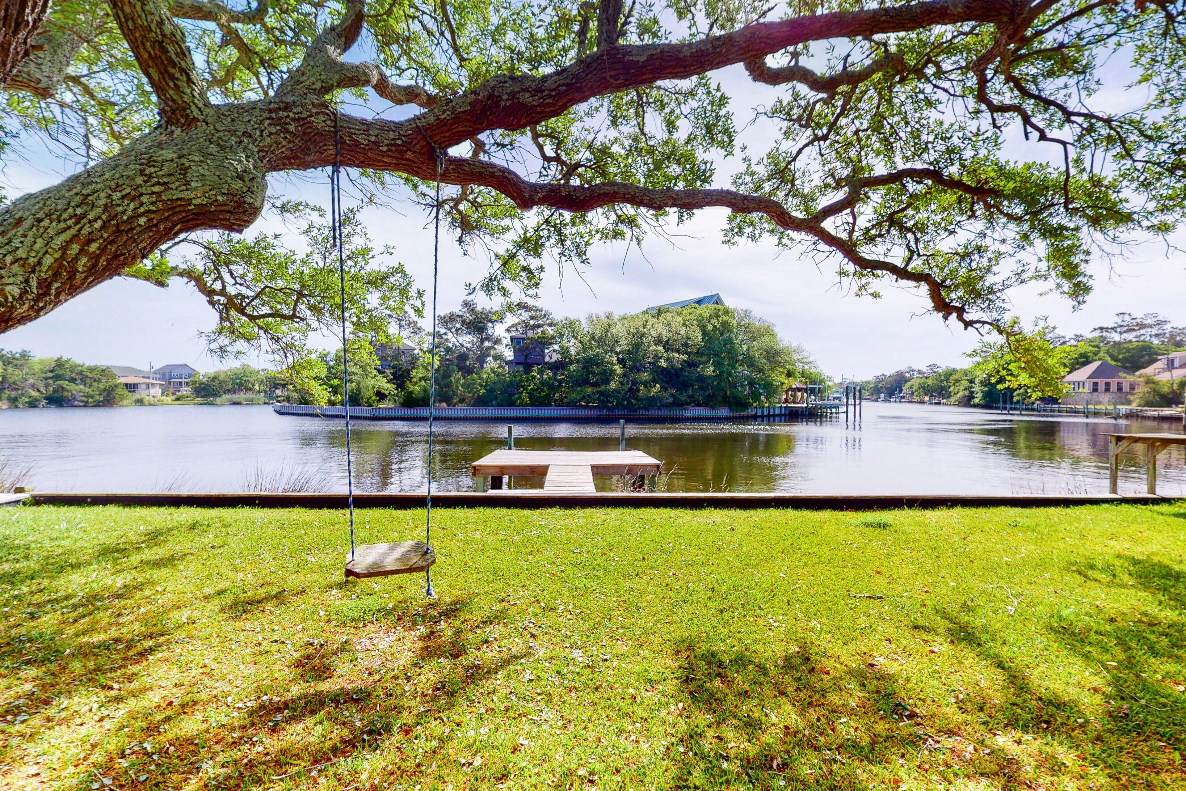 A lakeside park with a swing, a wooden dock, and a grassy area.