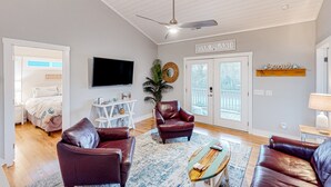 A spacious living room with leather sofas, a flat-screen TV, and a ceiling fan.