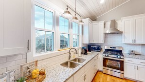 A modern kitchen with white cabinetry, a granite countertop, stainless steel appliances, and large windows.
