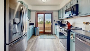 Une cuisine moderne dotée d’appareils électroménagers en acier inoxydable, de meubles de couleur turquoise et d’une grande porte-fenêtre coulissante donnant sur un balcon.