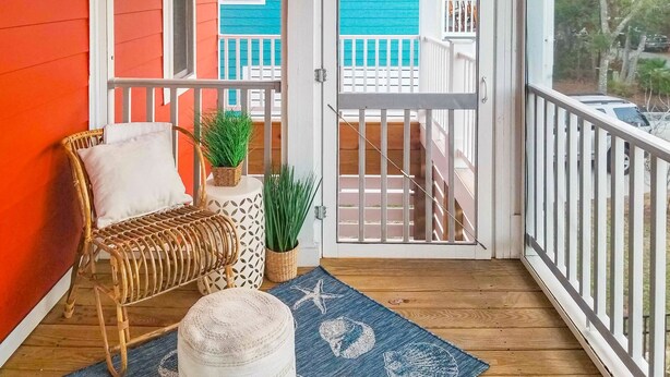 Une véranda avec un fauteuil en osier, une plante en pot et un tapis bleu orné d’étoiles de mer et de coquillages.
