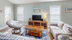 A living room with a sofa, a chair, a coffee table, a TV, and a cabinet. - Oak Island Oasis: Updated, dog-friendly home near the beach with fenced yard (Oak Island)