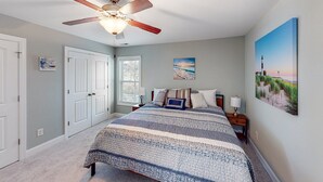A bedroom with a large bed, a ceiling fan, a nightstand, and a painting on the wall. - Oak Island Oasis: Updated, dog-friendly home near the beach with fenced yard (Oak Island)
