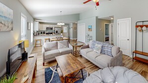 A spacious living room with a sofa, coffee table, and TV. There is a kitchen in the background with a dining area. - Oak Island Oasis: Updated, dog-friendly home near the beach with fenced yard (Oak Island)