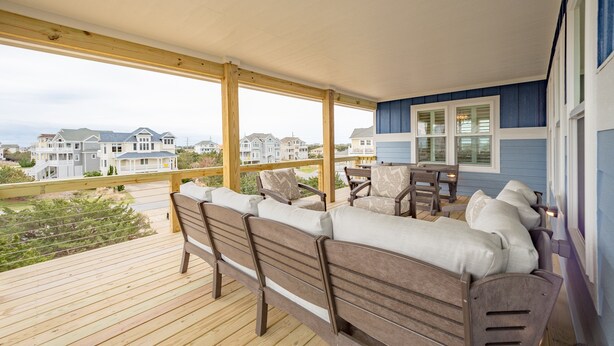 Eine Holzdielen-Terrasse mit einer Couch und Stühlen mit Blick auf eine Wohngegend.