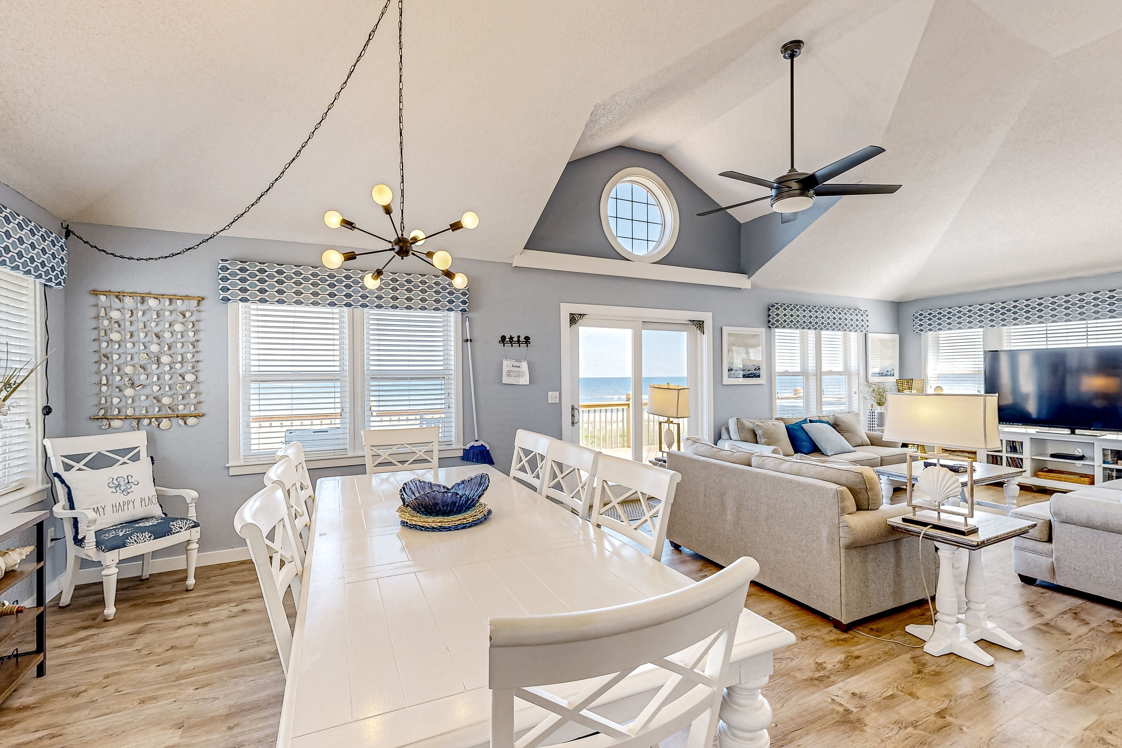 A spacious living area with a dining table, white chairs, a sofa, and a television.