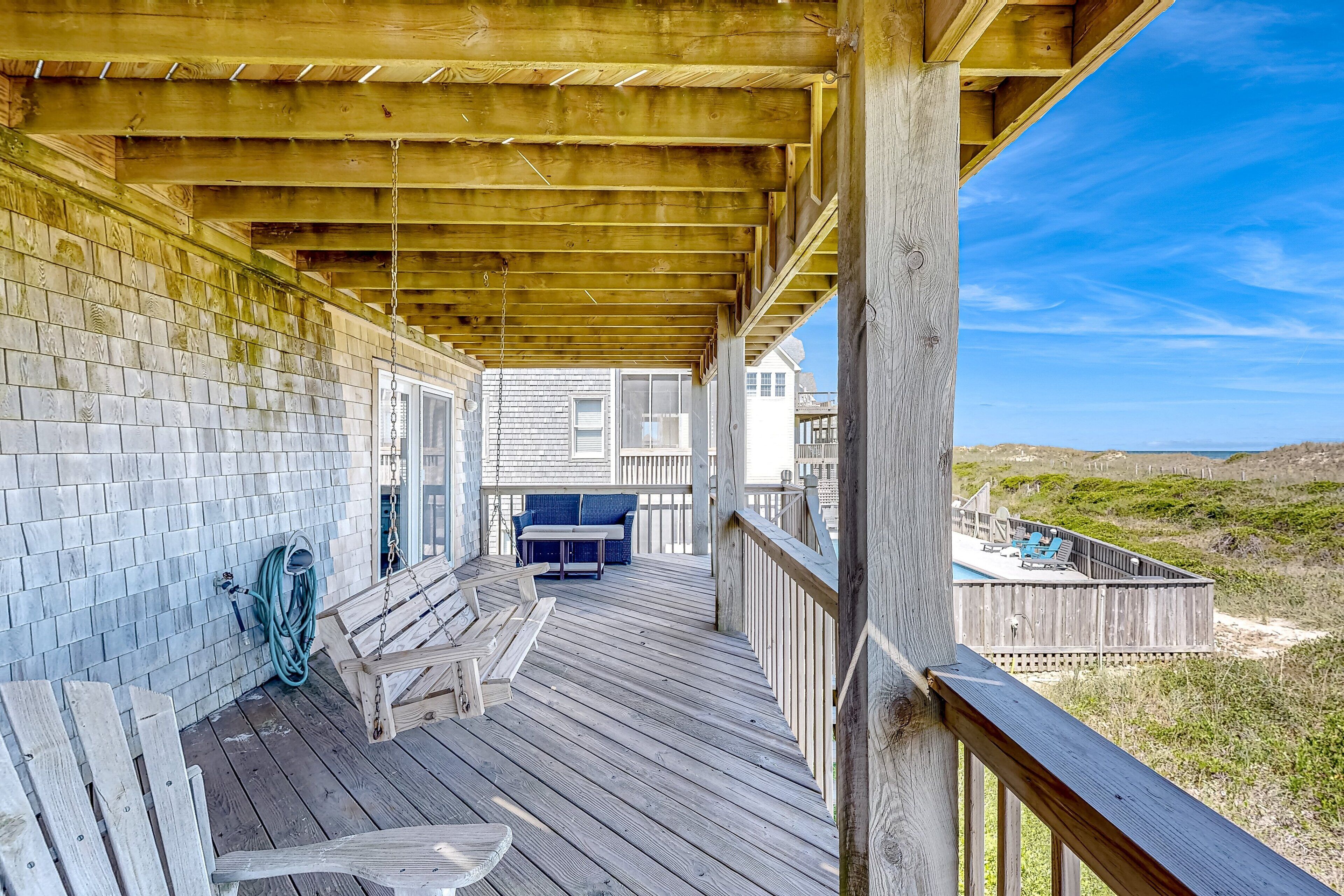 A wooden deck with a covered area, a pool, and a view of the beach.
