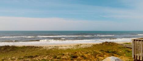 Vista de la playa con una terraza de madera y una duna.