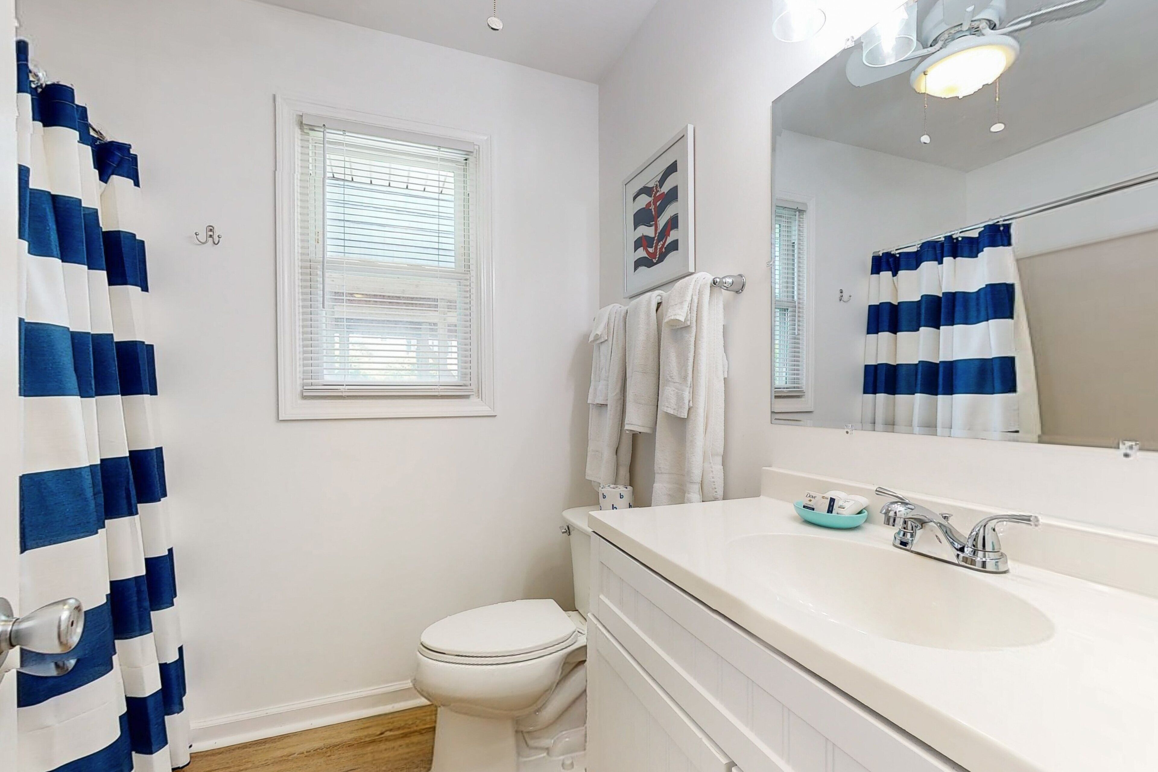 Un baño con inodoro blanco, lavabo con espejo y ventana con persianas.