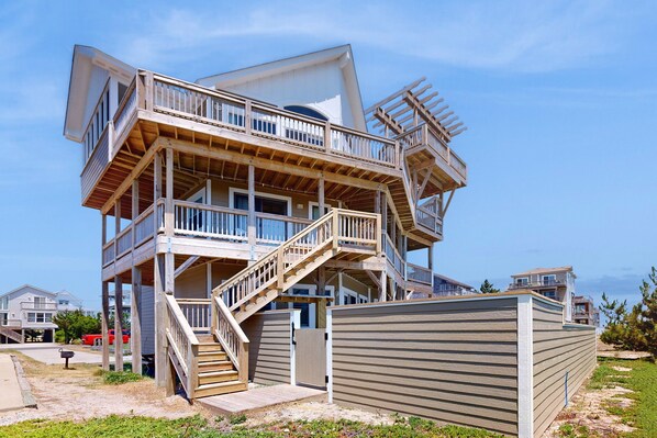 Een meerlaags huis aan het strand met houten balkons en een trap.