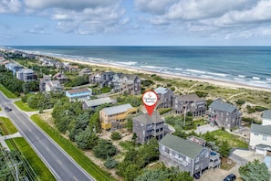An aerial view of a coastal residential area with houses, a beach, and a road.