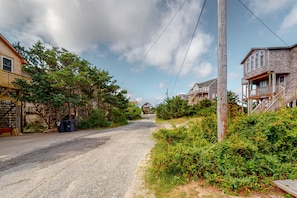 A residential street with houses on both sides, a gravel road, and a wooden utility pole. - Hooked on Beach Life #16-AC: Dog-Friendly, Ocean View, Shared Pool (Avon)
