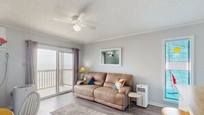 Una sala de estar con sofá, ventilador de techo, mesa y ventana con persianas.