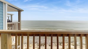 Una terraza de madera con vistas a una playa, con un edificio al fondo.