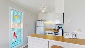 Una cocina con refrigerador blanco, estufa y alacenas, una encimera de madera y un ventilador de techo.
