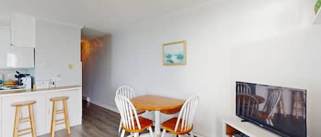 Cozinha moderna com armários brancos, uma mesa de jantar de madeira com quatro cadeiras, uma televisão e um pequeno espaço bar.