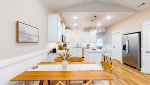 A modern kitchen with white cabinets, a wooden dining table, and a stainless steel refrigerator. - Pawsitive Island Escape: Dog Friendly, Fenced Yard (Oak Island)