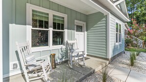 A house with a porch, two rocking chairs, and a small garden area with gravel and plants. - Pawsitive Island Escape: Dog Friendly, Fenced Yard (Oak Island)
