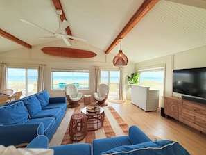 A spacious living room with a large sofa, two armchairs, a coffee table, a TV, and a ceiling fan.