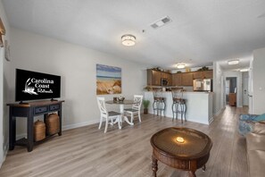 Un salon moderne comprenant un téléviseur, un coin repas, une cuisine et un espace salon confortable.