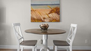A dining table with two chairs, a painting of a beach scene, and a bowl on the table. - Ocean view condo with a pool, hot tub, tennis, washer/dryer & central AC (North Topsail Beach)