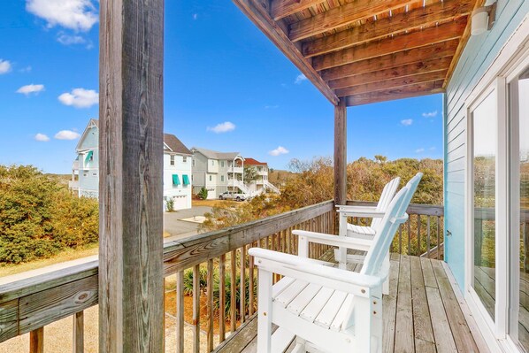 A wooden deck with white chairs, a covered area, and a view of houses in the background.