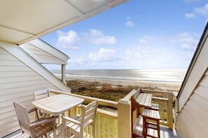 A balcony with a view of the beach, wooden furniture, and a wooden deck. - Pelican's Penthouse:  Snowbird friendly top-floor condo with ocean view balcony (Caswell Beach)
