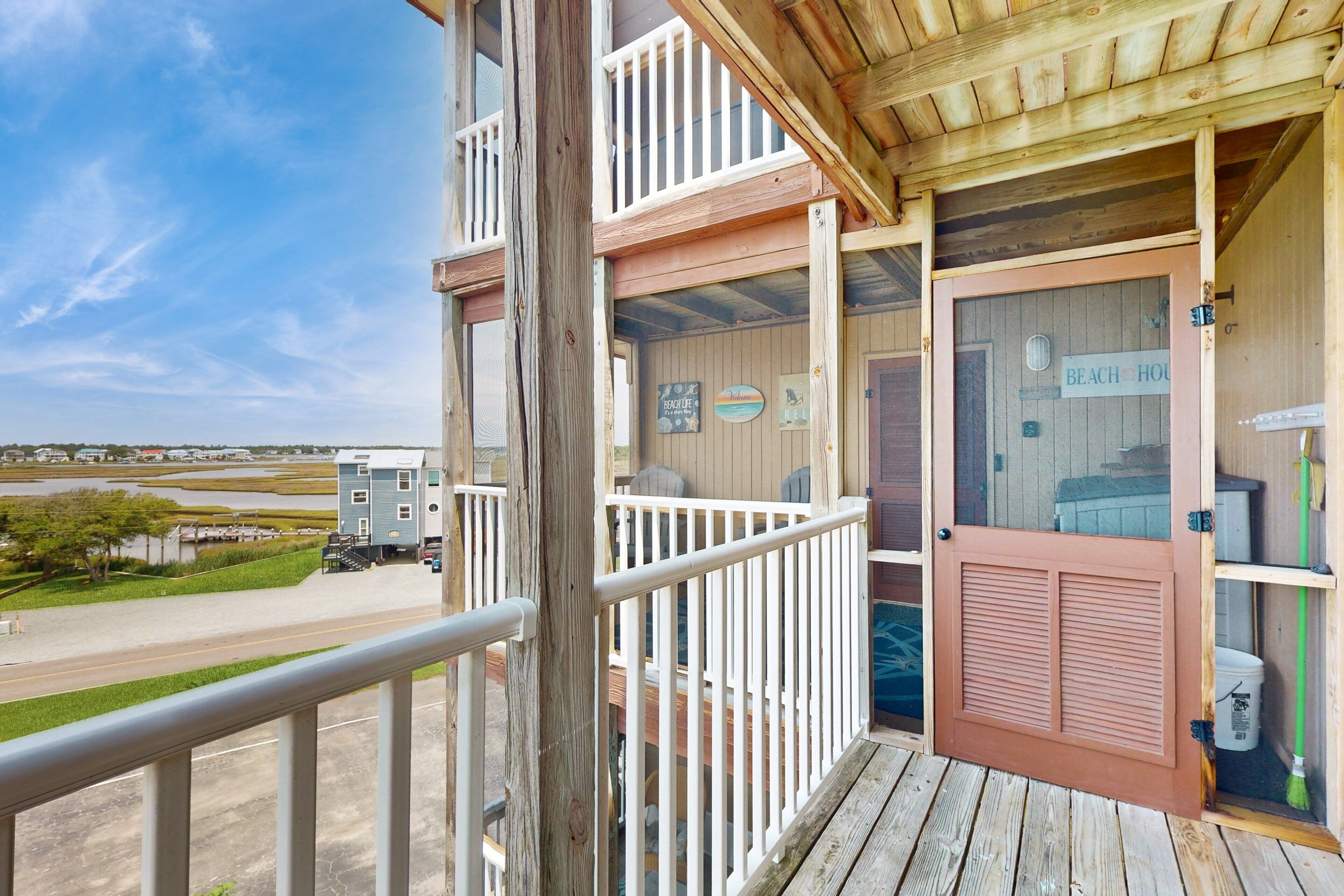 A wooden balcony with a view of a beach house and a road.