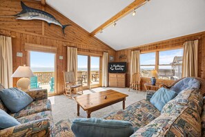 Un intérieur en bois, avec un grand poisson décoratif fixé au plafond, un canapé, une table et une enseigne indiquant « Hatteras Beach ».