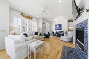 Uma sala de estar espaçosa com um sofá branco, uma mesa de jantar e uma lareira.