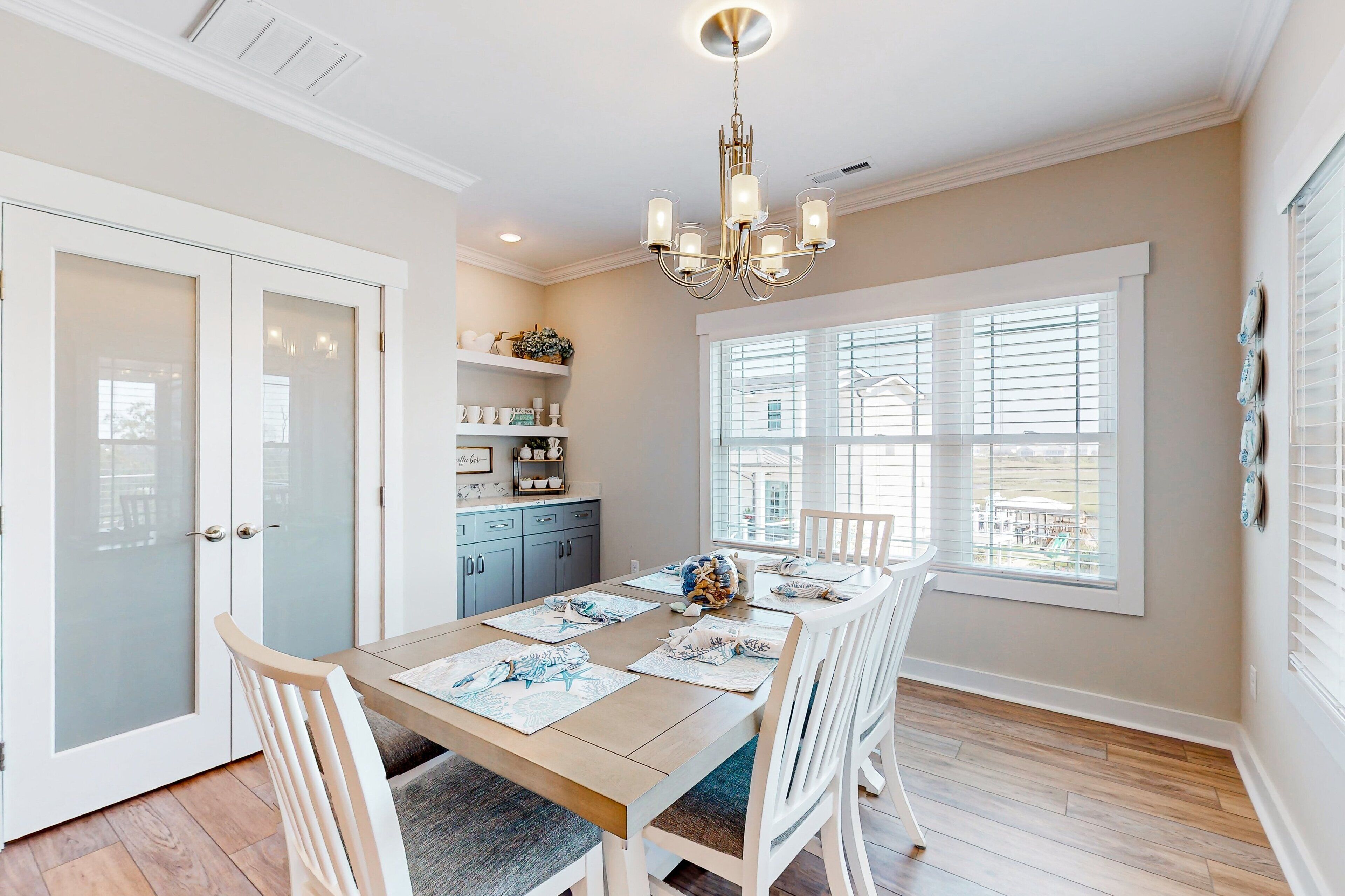 A dining area with a table set for four, a chandelier, and a view through the window.