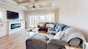 A spacious living room with a large sectional sofa, a flat-screen TV, and a fireplace. - A Shore Thing: Water Views, Pool, Dock (Oak Island)