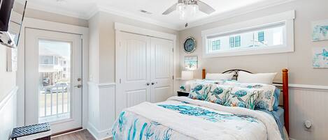 A bedroom with a bed, a ceiling fan, a window, and a door.
