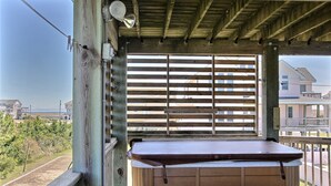 A wooden deck with a hot tub, a wooden railing, and a view of the ocean and houses. - Dog-friendly house with AC, W/D, private pool, & hot tub (Waves)