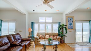 A spacious living room with a leather sofa, a glass coffee table, and a ceiling fan. - Oceanfront home with beach access, pool, washer/dryer, central AC (North Topsail Beach)