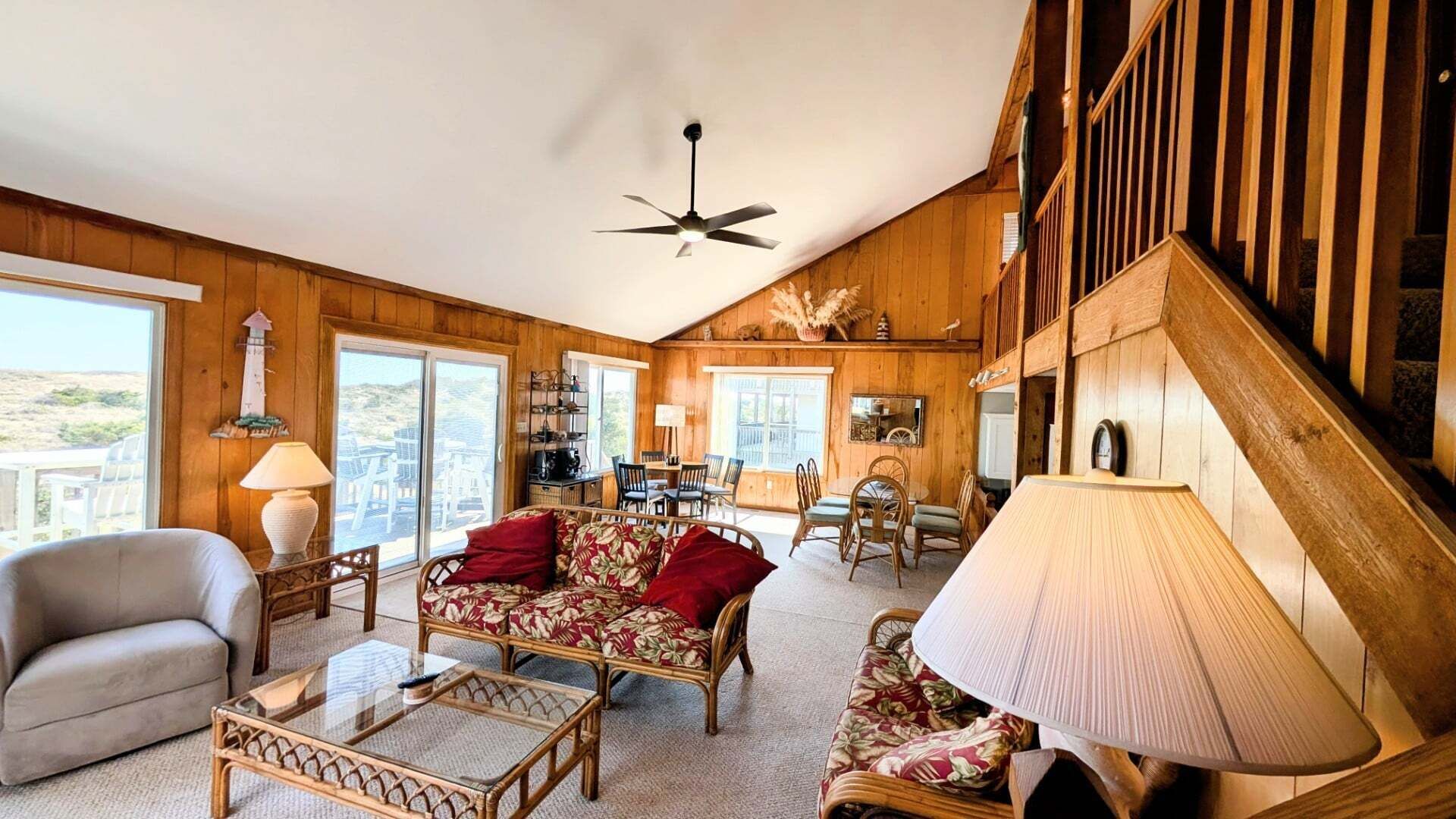 A spacious living room with a high ceiling, wooden walls, and a dining area with wicker furniture.