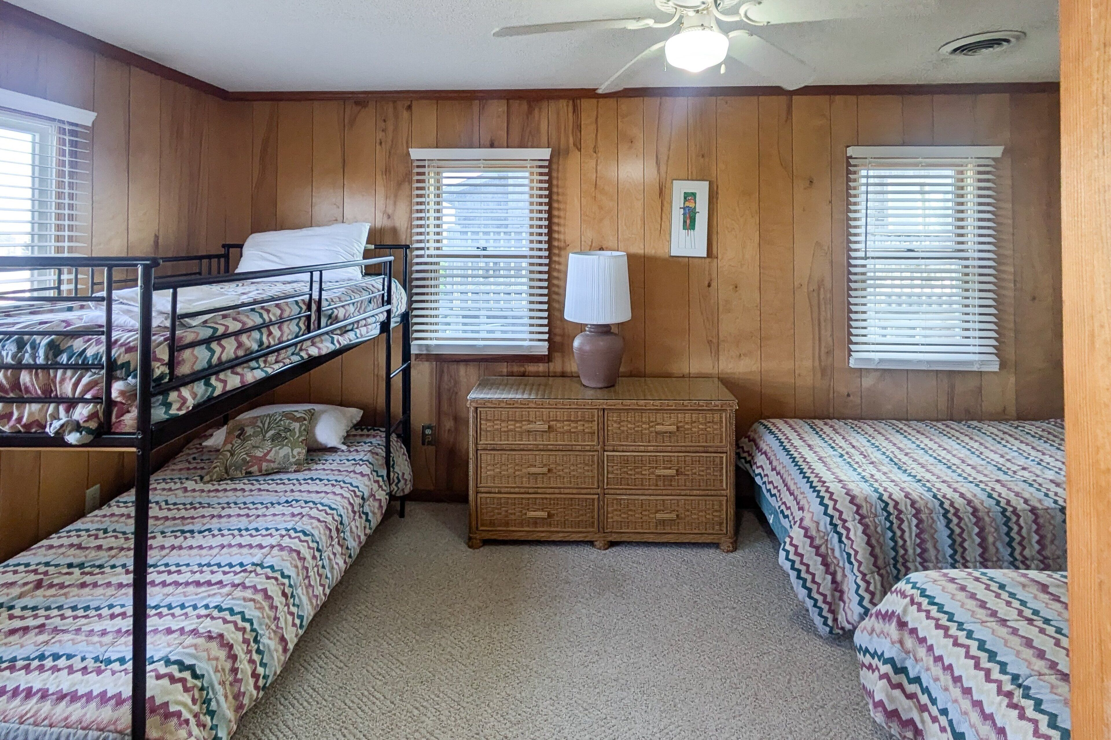 A room with bunk beds, a dresser, and two windows with blinds.