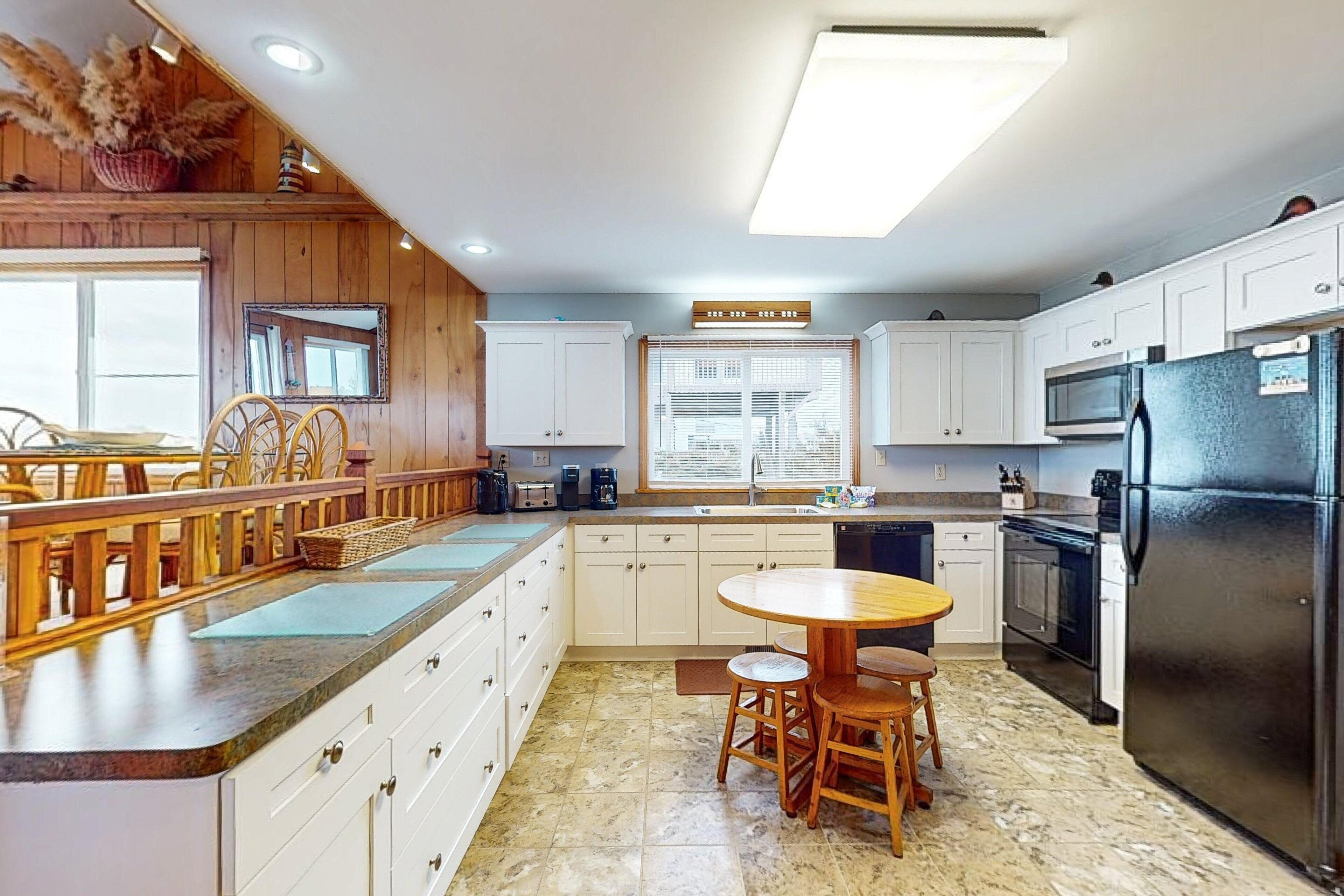 A modern kitchen with white cabinets, a central island with stools, a built-in oven, and a stainless steel refrigerator.