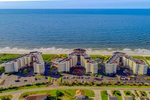 A coastal hotel with multiple buildings, parking areas, and a view of the ocean.