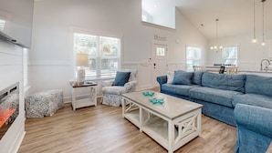 A spacious living room with a wooden floor, a blue sofa, a patterned armchair, and a white coffee table. - Knee Deep: Family friendly, near beach (Oak Island)