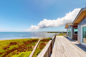 A wooden deck overlooking a beach with a clear view of the ocean and a large cloud in the sky.
