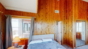 A wooden-paneled room with a bed, a nightstand, a lamp, and a mirror. - Waterfront House w/ Sound View, Shared Pool, Private W/D, Private Hot Tub (Frisco)
