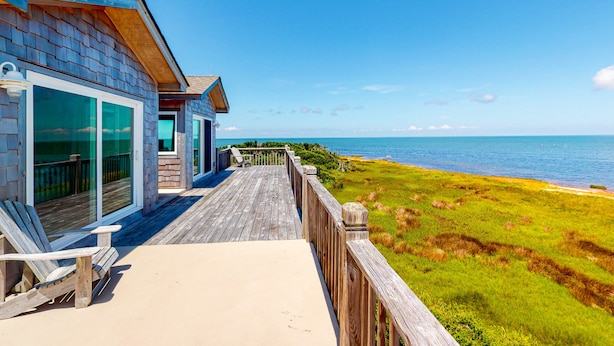 A wooden deck with a view of the ocean, a glass door entrance, and a bench. - Waterfront House w/ Sound View, Shared Pool, Private W/D, Private Hot Tub (Frisco)