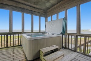 Une terrasse en bois avec un jacuzzi et un banc, donnant sur une étendue d’eau.