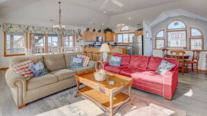 Un salon spacieux avec un plafond haut, un canapé rouge, un canapé beige et une table basse en bois.