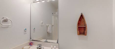 Een badkamer met een wastafel, spiegel, verlichting boven de spiegel, een handdoekhouder en een houten plank.