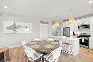 A modern kitchen with white cabinetry, stainless steel appliances, and a dining area with a round table and wicker chairs.