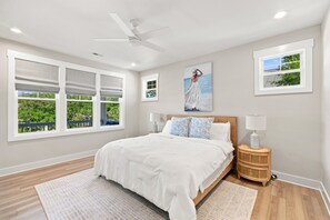 A bedroom with a bed, two bedside lamps, a ceiling fan, and large windows with blinds.